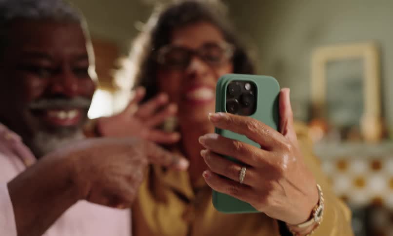 An african american woman and man wave at a cell phone with a green case are video chatting