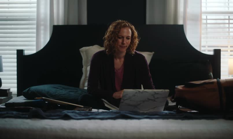 Woman sitting on her bed works on a laptop and then makes a note