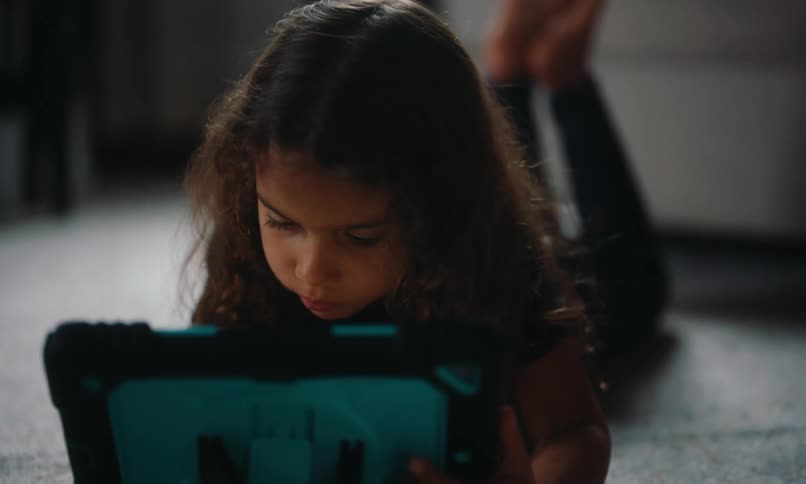 Little girl lying face down on the carpet interacting with a tablet