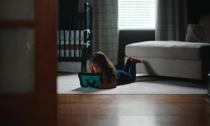 Little girl lying face down on the living room rug and interacting with the tablet in front of her