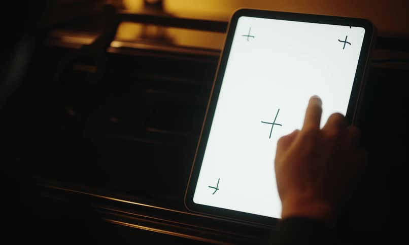 A hand is interacting with a tablet screen displaying a white background with black crosshairlike symbols in each corner and one in the center