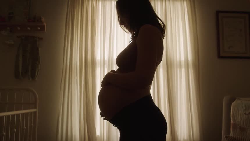 Pregnant woman in a bedroom facing a crib running her hands over her belly