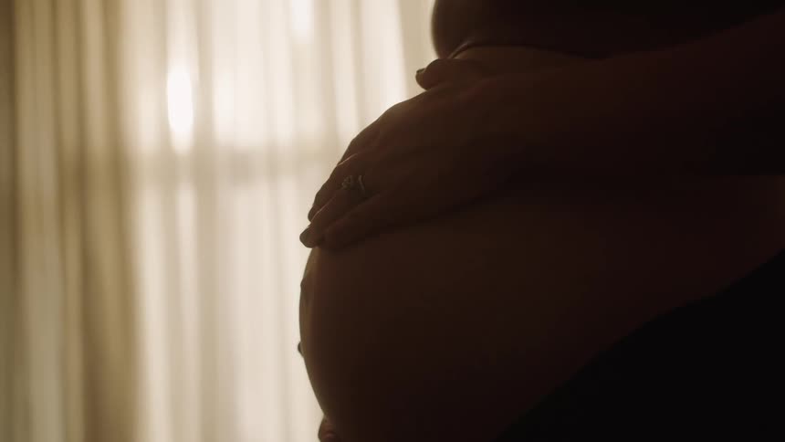 Silhouette of a pregnant mother running her hands over her belly