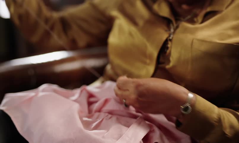 Pair of hands sewing a pink shirt by hand