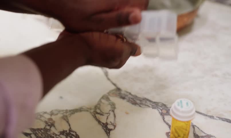 Pair of hands taking several capsules from a container with dividers and taking them