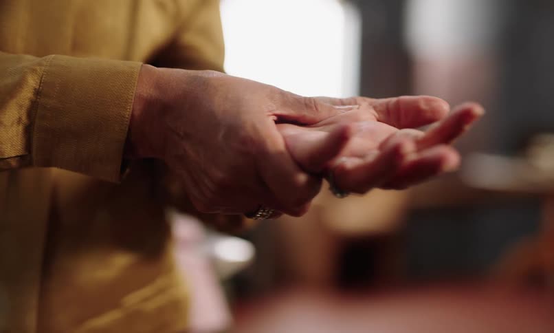 Woman massages one of her hands while standing indoors at home on a sunny day