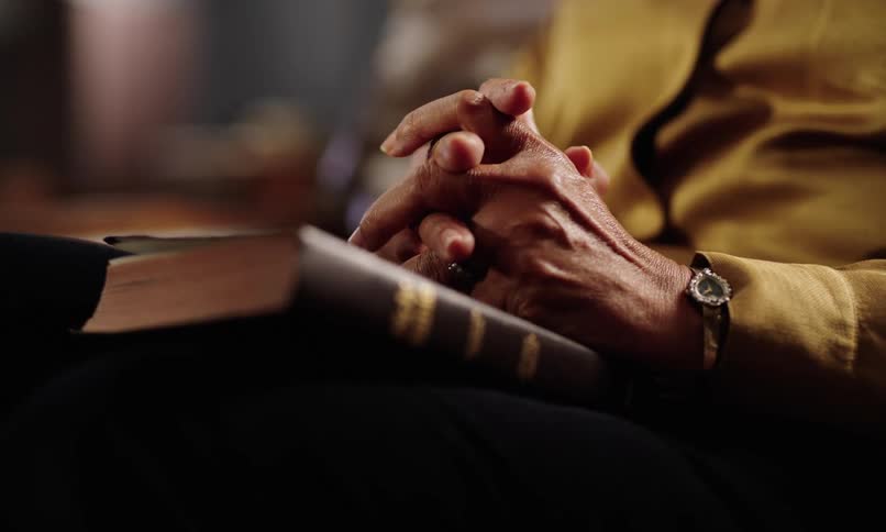 A persons hands with fingers intertwined and in front of a closed brown book