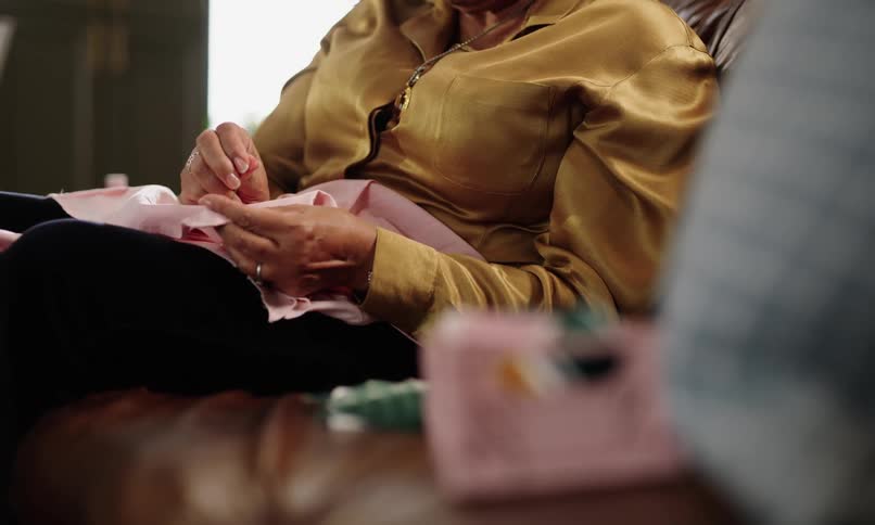 A person in yellow clothes is sewing something on a pink fabric