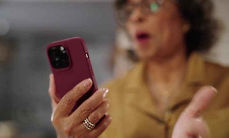 A person holding a cell phone with a red case while talking and looking at it