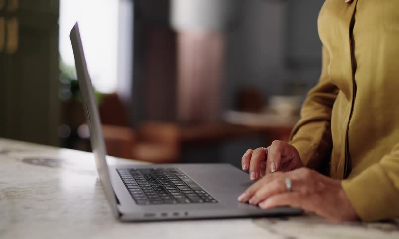 An elderly person wearing a yellow shirt is working on a laptop with a blurred background