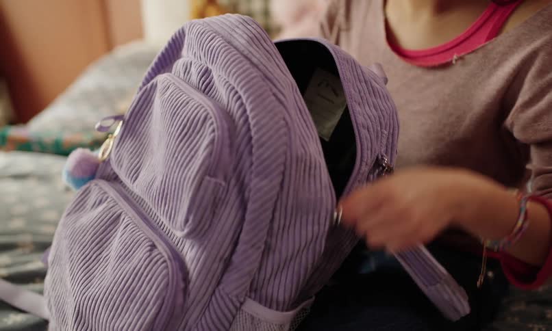 Teenage girl packs her schoolbag while sitting on the bed