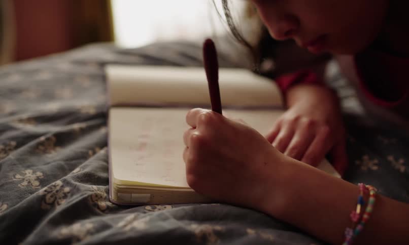 A girl with a colorful beaded wristband writes in a notebook