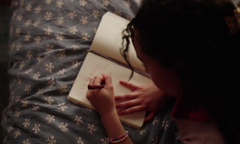 Teenage girl writes in her journal while lying on her bed