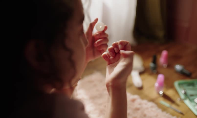 Teenage female applies fingernail polish to her nails while at home during the day