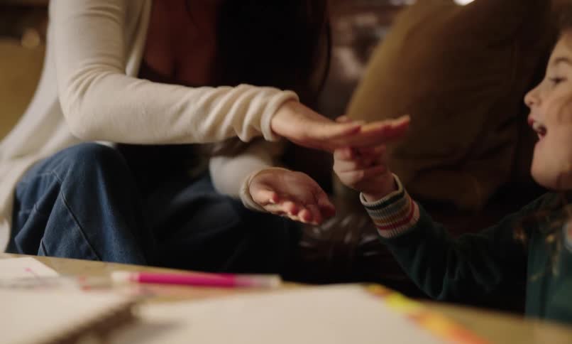 A little girl playing rock paper scissors with an adult standing next to her