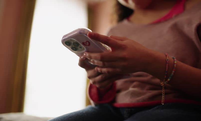 A teenager is holding a smartphone with a white case that has a red heart on it wearing a beaded bracelet on the wrist