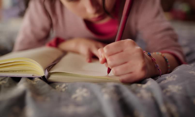 Little girl lying in bed writing in a book