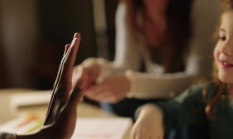 A girl gives a highfive to an adult in a room where people are drawing on paper