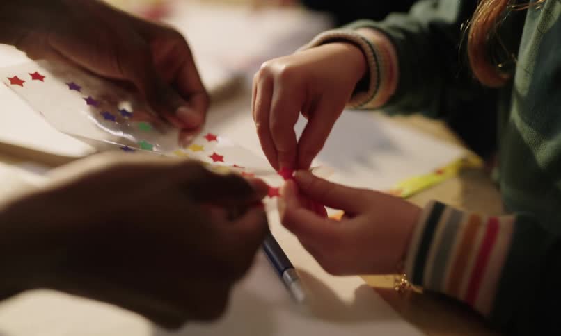 A persons hand helping a child remove stickers from a transparent sheet