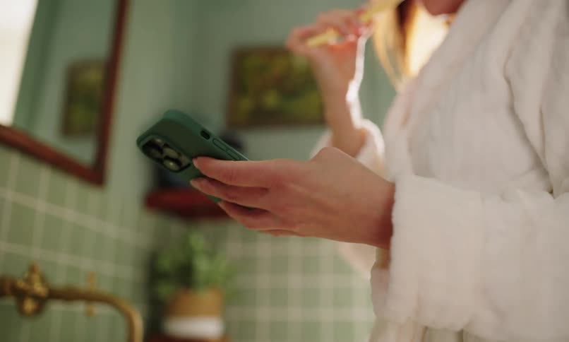A woman is using her cell phone while brushing her teeth