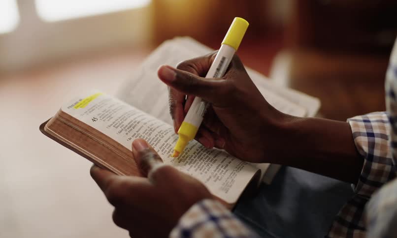 Pair of hands with highlighters using on passages from a bible