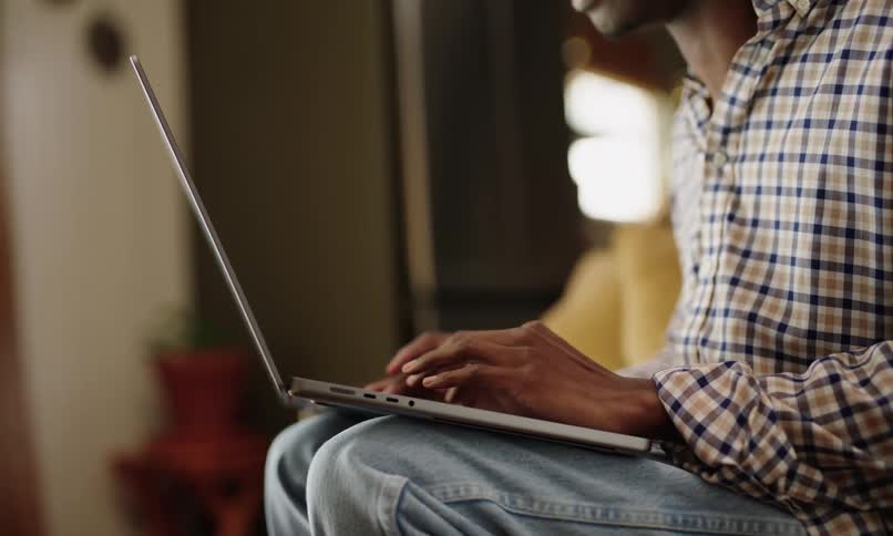 A person wearing a checkered shirt and jeans is sitting and typing on a laptop