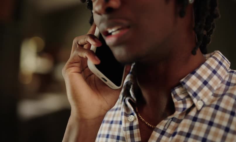 A teenager wearing a checkered shirt is holding a smartphone to their ear engaged in a phone call