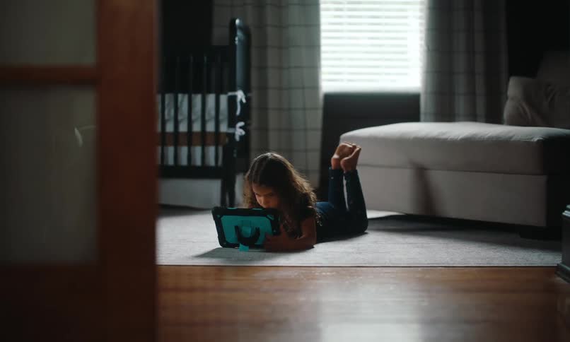 Girl entertains herself while lying face down on the living room carpet using a tablet