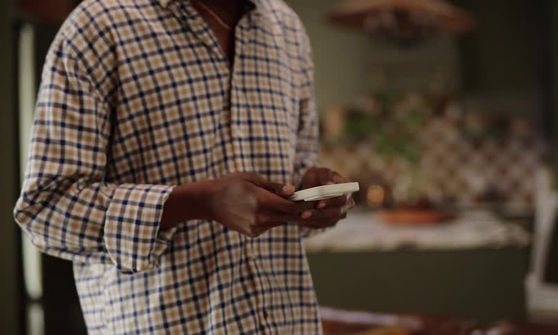 A person wearing a checkered shirt and jeans is walking while typing on a phone