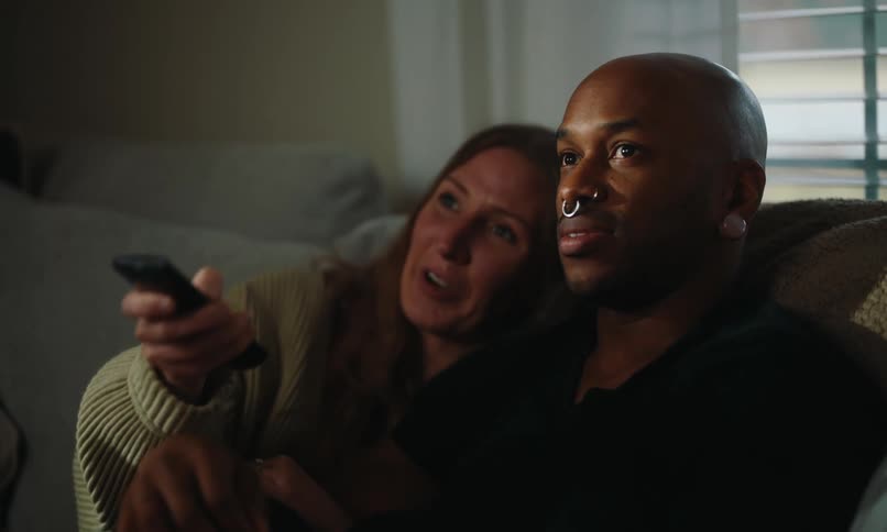 Man and woman cuddle together on the couch while watching television
