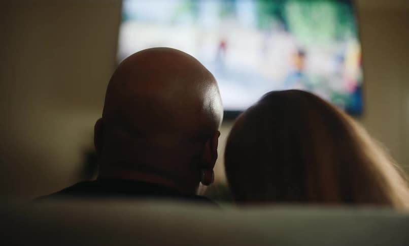 Couple sitting on a sofa watching television seen from behind