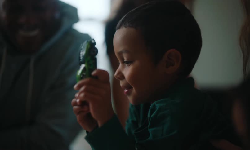 A mother smiles as her son plays with a toy car