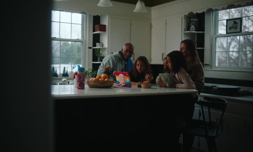 Family gathered in the kitchen sharing a happy moment around an electronic device