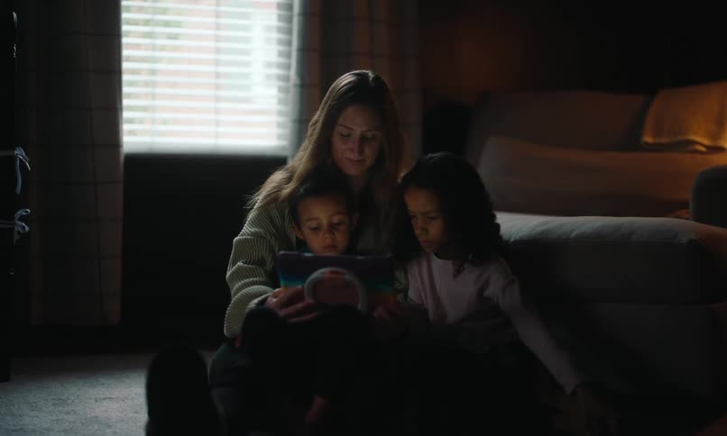 A mother and her children are sitting and lookin at a tablet