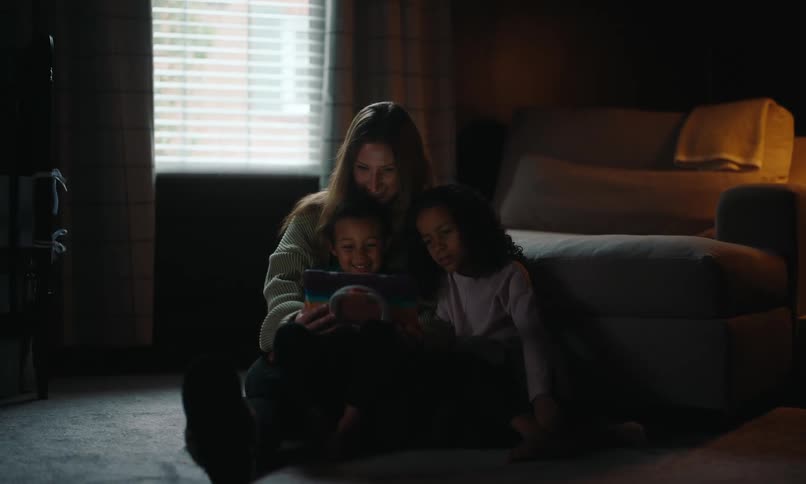 Mother son and daughter watch a tablet in a dimly lit room
