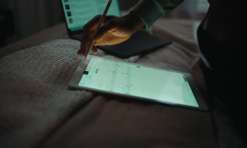 Man sitting on bed playing guitar and interacting with a tablet next to him