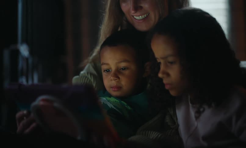 Mother and her children enjoy watching an entertainment on a tablet in a dimly lit room