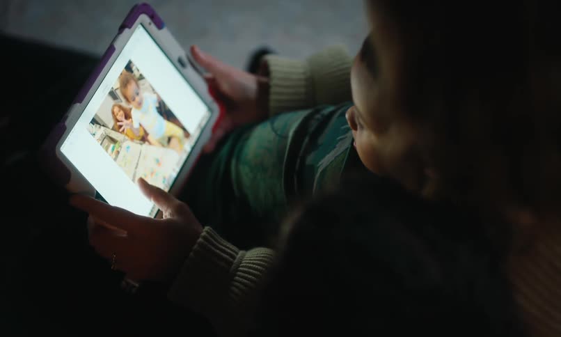 Mother and her children cuddle together while viewing photographs on a tablet