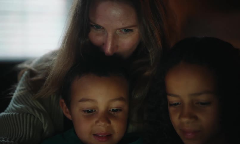 Mother cuddles with her children while they watch a video on a tablet
