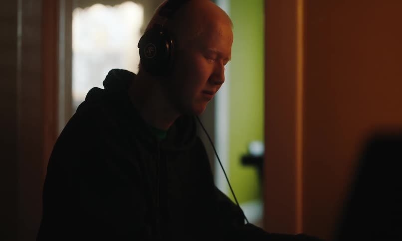 A man with his eyes closed wearing headphones is listening to music in a dark room
