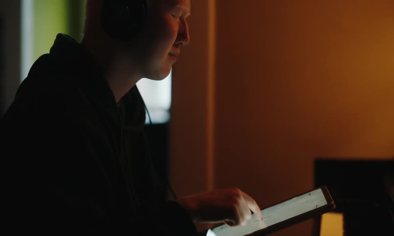 Man sitting in front of a piano interacting with a tablet
