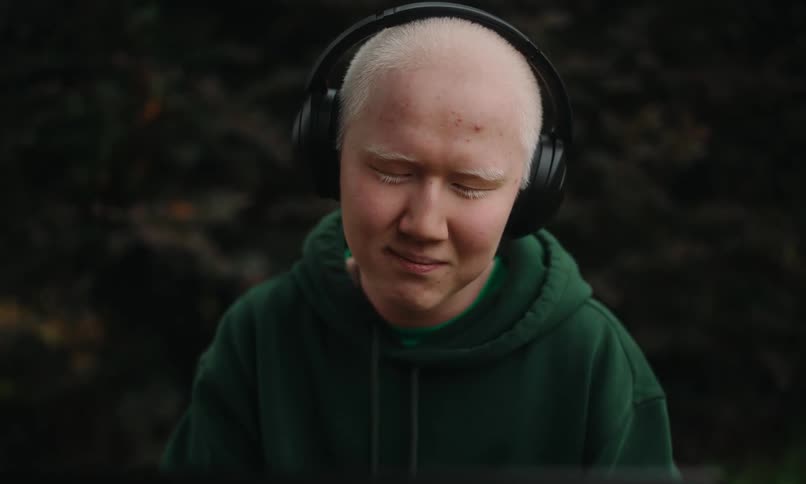 Portrait of a young man with headphones sitting outdoors and facing a laptop