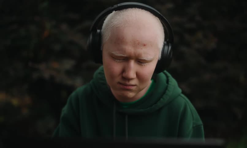 Portrait of a young blind man with headphones sitting outdoors