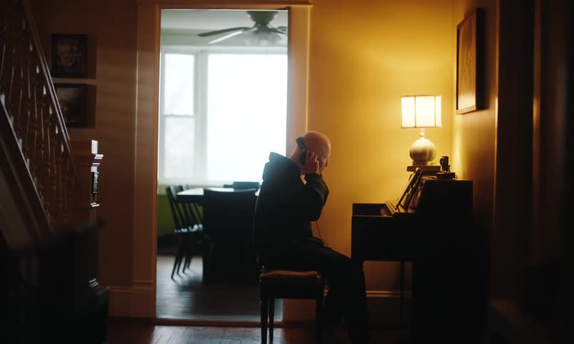A man in a black hoodie wears headphones and plays the piano in the room