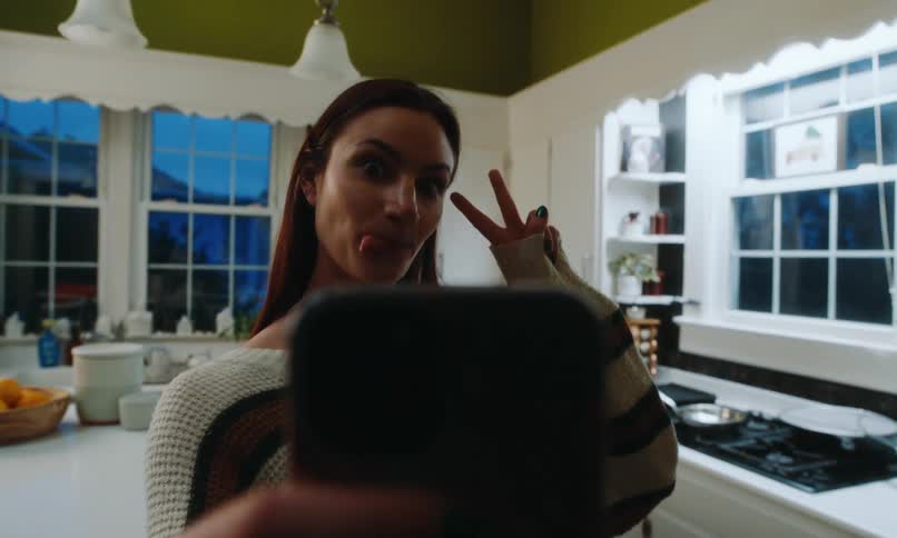 Woman makes a face while taking a selfie in her kitchen in the evening