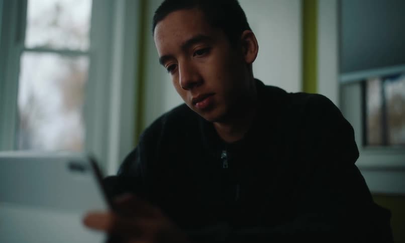 A young man wearing a black shirt uses a smartphone and a tablet in his room