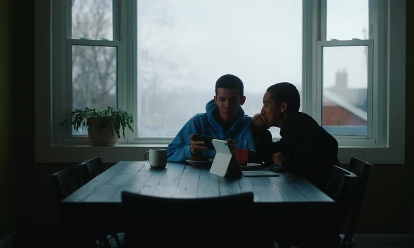 Two young people sitting at a table interacting with a smartphone and a tablet