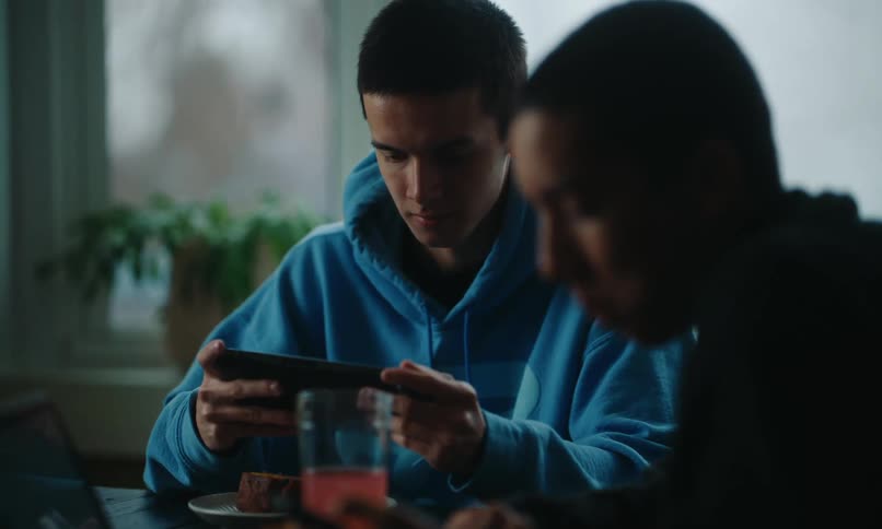 One brother scrolls on his smartphone while another plays a game during meal time