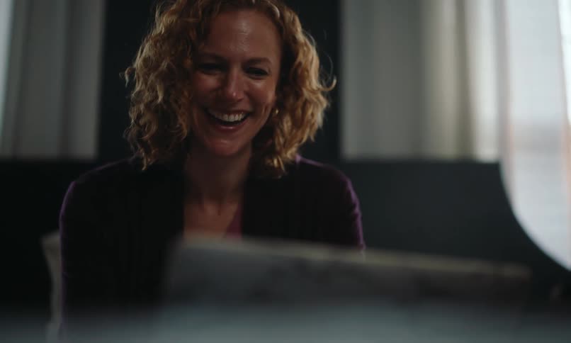 The face of a woman laughing at a laptop while sitting on a sofa