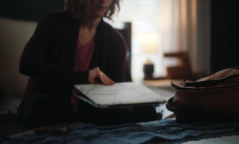 Red-headed woman with curly hair takes laptop out of yellow bag and opens it in a room